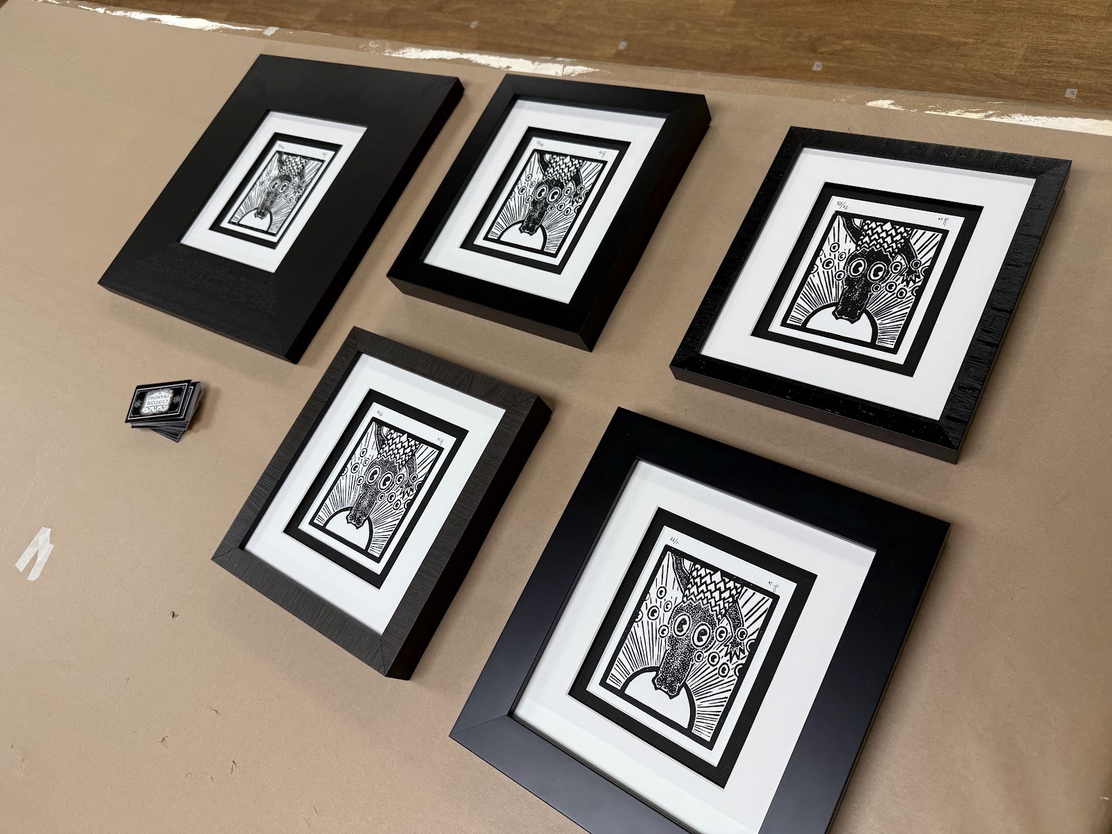 Completed custom-framed black-and-white art laid out on a frame shop worktable